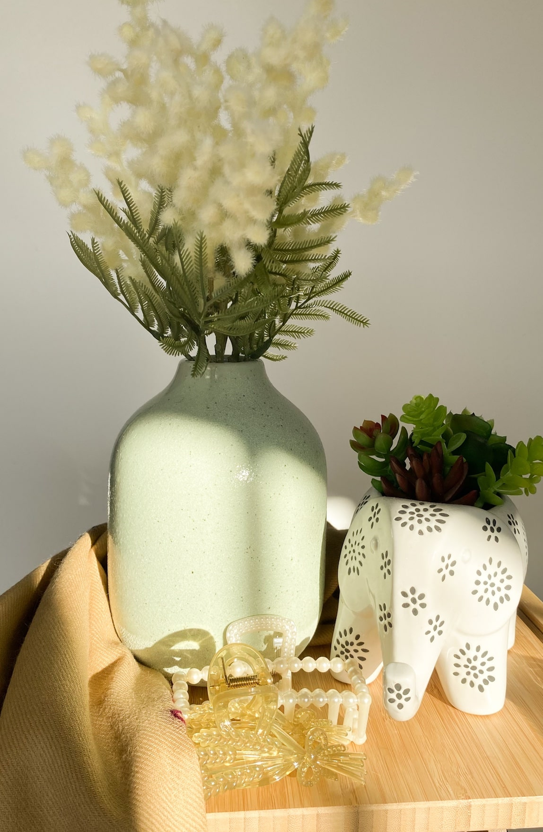 green vase with white flowers on a brown shelf next to an elephant ornament