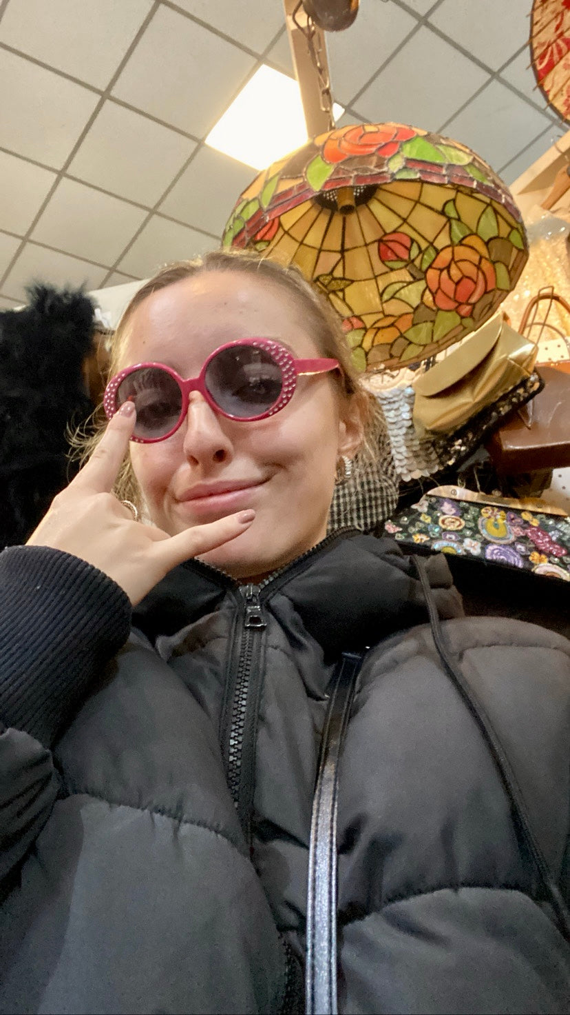 female taking a selfie wearing a pair of pink sunglasses and wearing a black coat
