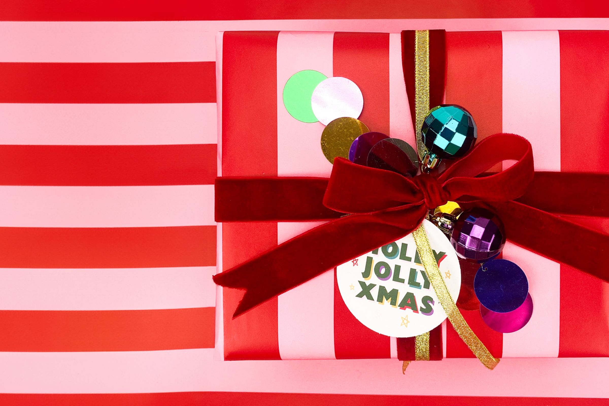 wrapped christmas present wrapped in pink and red striped wrapping paper with red bow and disco ball baubes