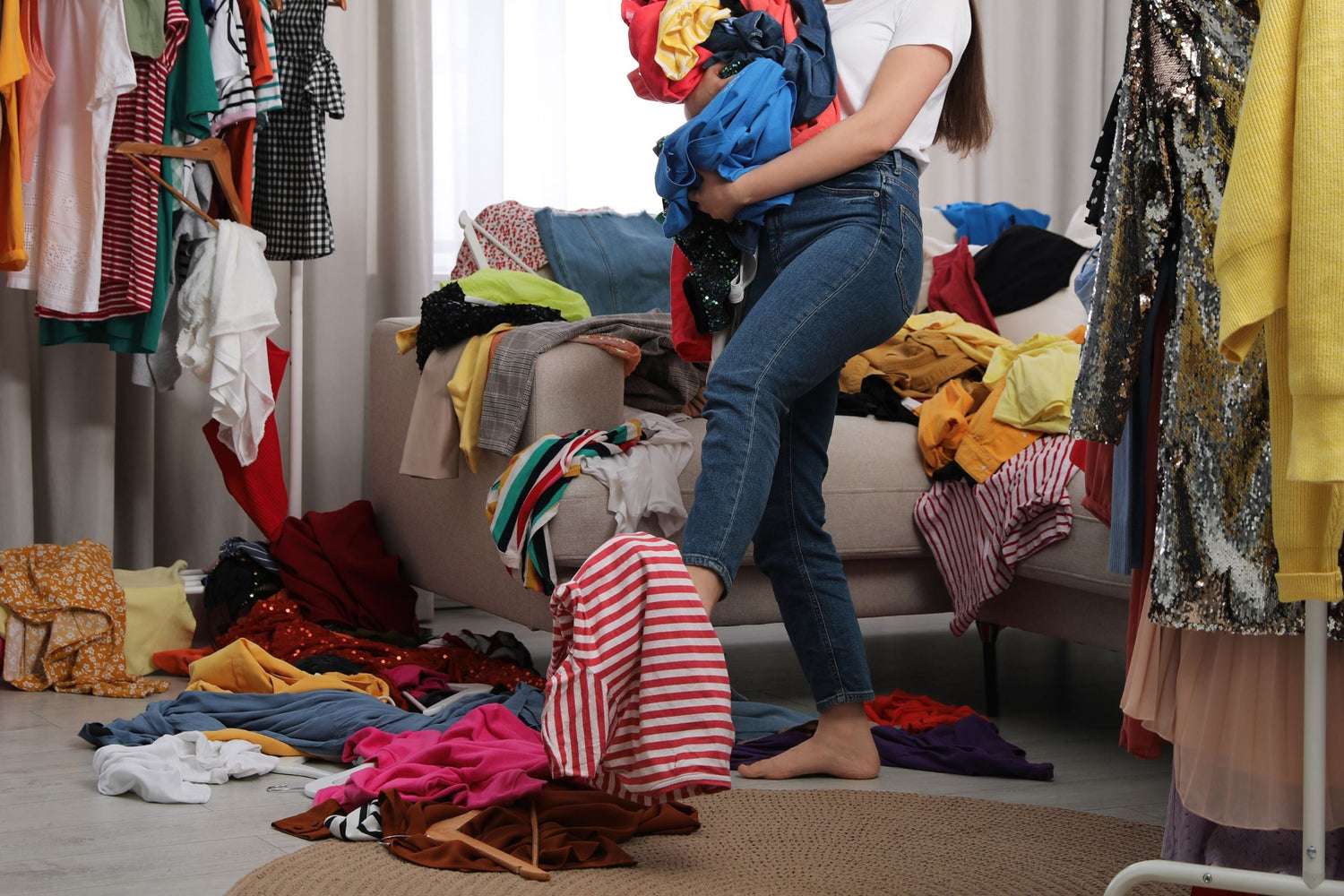 a woman in room with lots and lots of womens clothing all around the room, she is also holding lots of clothes too