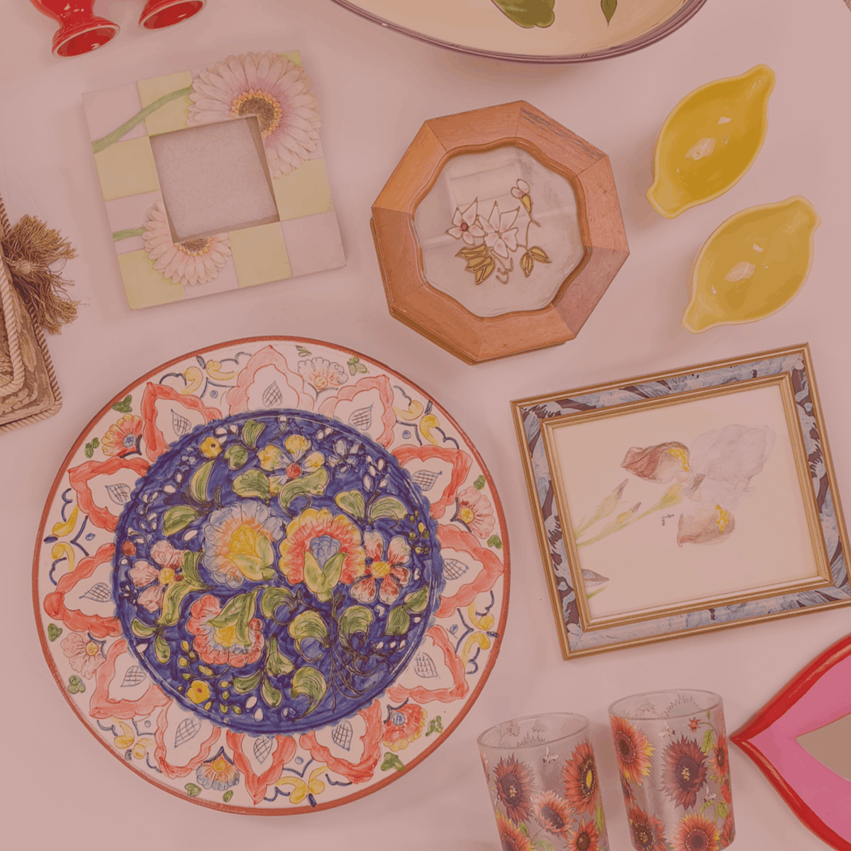 Decorative items including a floral plate, framed pictures, and glasses on a white surface.