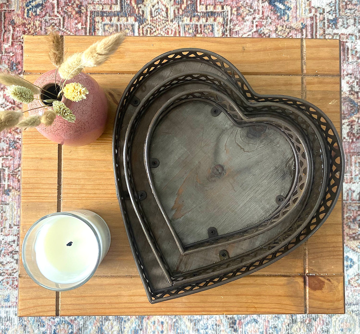 Heart shaped wooden trays viewed from above, laid flat on a wooden side table with a white candle also on the side table