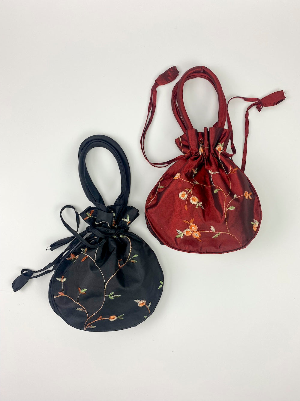 a black and a red satin draw string bags with floral detail on a white background