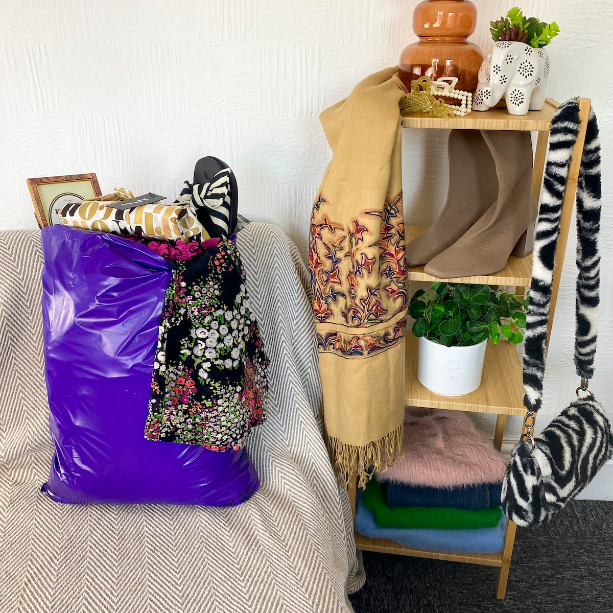 Womens clothes filling a purple mailer bag which is sitting on a chair next to shelves that have shoes, clothes, bags and ornaments on it